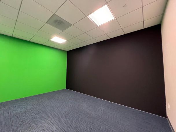 Empty room with one bright green wall and one black wall, likely used for video production or media creation.