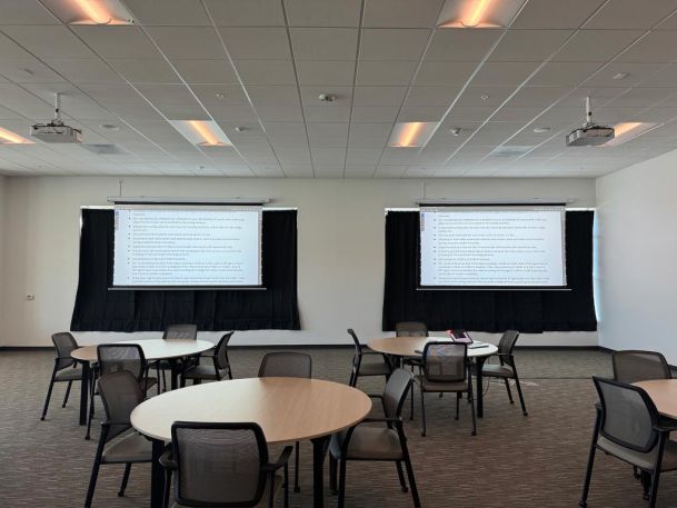 Presentation room with round tables, two projection screens, and mounted projectors.