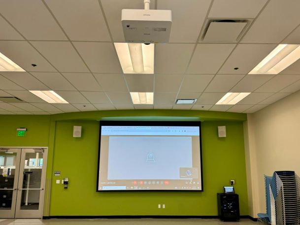 Room for presentations with a green accent wall, a ceiling-mounted projector, and a large projection screen.