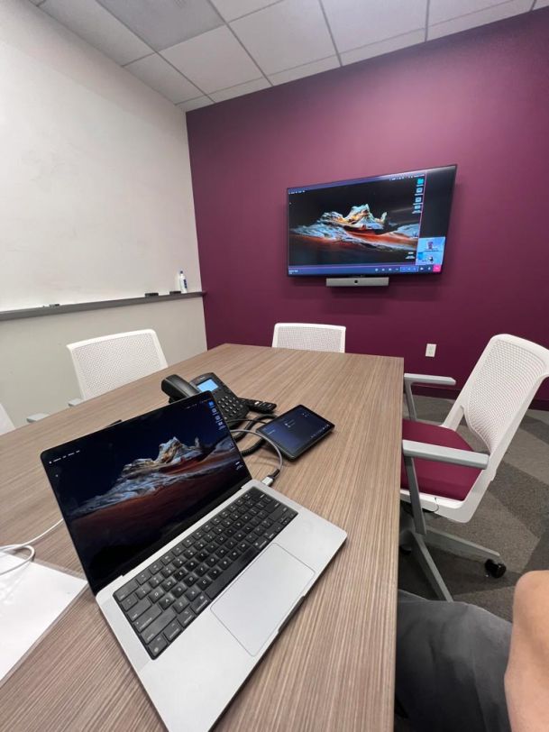 A conference room with a laptop, a large wall-mounted screen, and a dark purple accent wall.