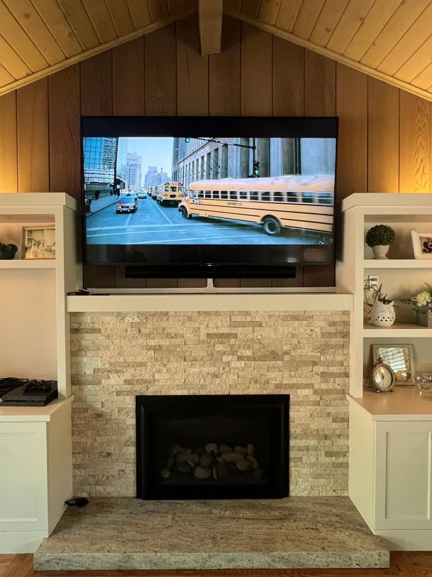 A flat-screen TV mounted above a stone fireplace in a cozy living room, showing a scene of yellow school buses in a city.