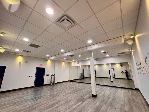 Fitness or dance studio with mirrored walls, ceiling lights, and hardwood floors.