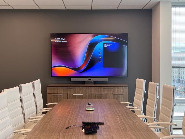 Modern conference room with white leather chairs, a wooden table, and a large wall-mounted display showing a vibrant screen.